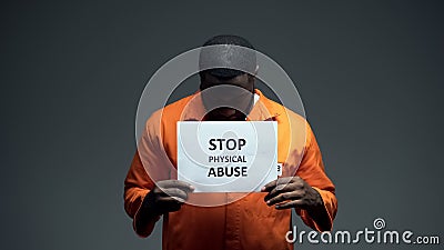 Black male prisoner holding stop physical abuse sign in cell, sexual harassment Stock Photo