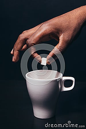 Black man hand hold cube of sugar above white cup Stock Photo