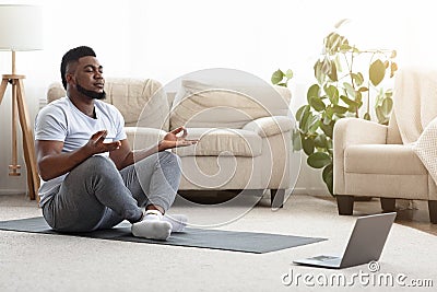 Black Man Meditating In Front Of Laptop, Practicing Yoga At Home Stock Photo