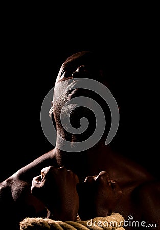 Black man in shadows with hands bound with rope. Stock Photo