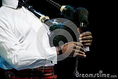 A black man in a white shirt plays the Scottish bagpipe. Multicultural Stock Photo