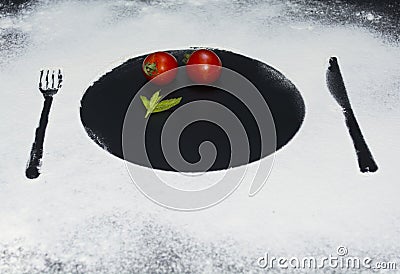On a black marble background flour powder powdered snow silhouette plate plate fork knife appliances in the center tomato and mint Stock Photo