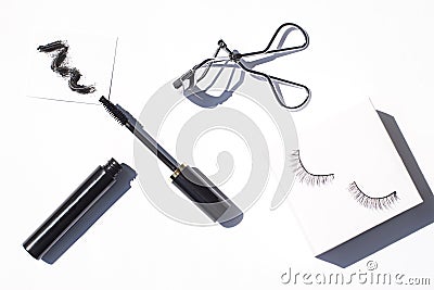 Black mascara close up with brush strokes, an eyelash curler and false eyelashes on the white background. Stock Photo