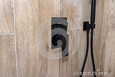 Black, matt metal shower faucet protruding from the tiled wall, imitating wood. Stock Photo