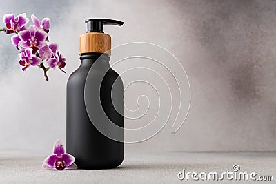 Black matte bottle with a wooden pump cap and vibrant purple orchid flower for spa-like atmosphere Stock Photo