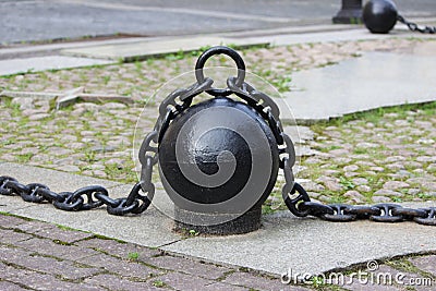 Black metal chain with large links and round heavy weights lies on concrete slabs on the ground. Stock Photo