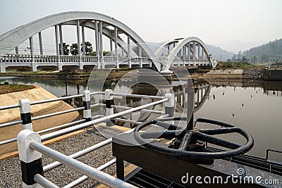 Black metal cogwheel controlling floodgate with texts in Thai language meaning `the property of`, and the view of white concrete r Stock Photo