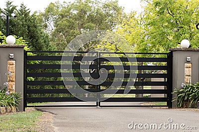 Black metal driveway entrance gates set in fence Stock Photo