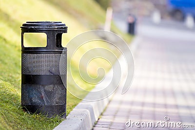Black metal garbage bin in park with blurred sunny background Stock Photo