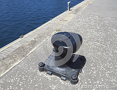 Black metal mooring bollard in marina and port terminal. Close up of mooring noray on a dock. Port conditioning Stock Photo