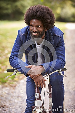 Black middle aged man sitting on a bike in a park, leaning on the handlebars smiling, front view, close up Stock Photo