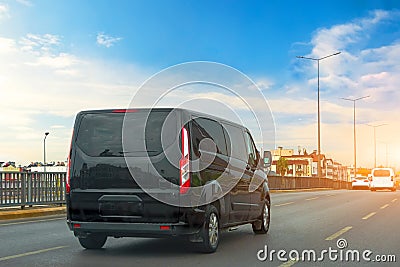 Black modern passenger charter van with a small delivery moves fast on the highway to the urban suburbs. Business distribution and Stock Photo