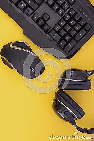 Black mouse, the keyboard, the headphones are isolated on a yellow background, the top view. Flat lay Stock Photo