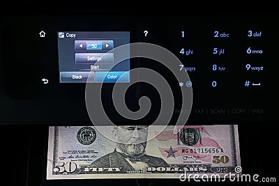 Black multifunction printer with touch screen display makes copy of 50 dollar bill in the dark. Printing money. Stock Photo