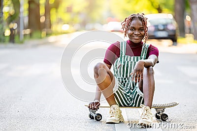 Black non-binary person with a skateboard sitting on the street Stock Photo
