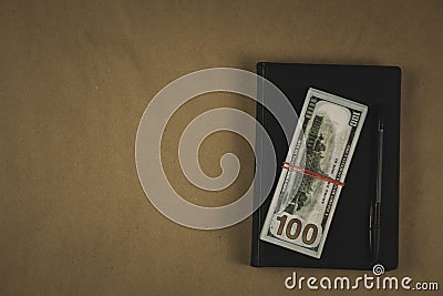 A black notebook , a pen and dollar cash banknotes on wooden background - concept of financial management or planning, make money Stock Photo