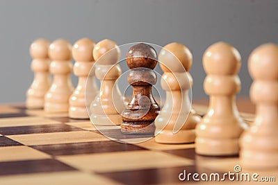 A single black pawn is placed among other white pawns Stock Photo