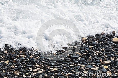 Black pebbles on the seashore washed by the sea wave. Sea coast in the resort of the island of Cyprus Stock Photo