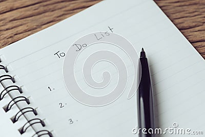 Black pen on what to do in personal to do list note pad on wooden table using as task list, things to complete and project check Stock Photo