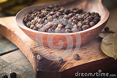 Black pepper in a spoon lies on a cutting board near the bay leaf on a background of blue boards Stock Photo