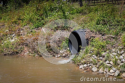 Black plastic drainage culvert pipe releasing water into a stream, environmental safety issue Stock Photo