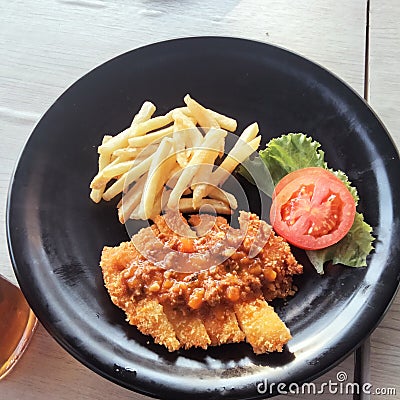 A black plate of chicken katsu with the french fries and the topping is tomato and salada Stock Photo