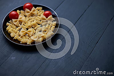Black plate with ripe and juicy cherry tomatoes and different types of raw pasta Stock Photo