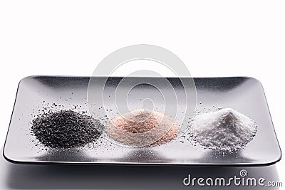 On a black plate are three types of salt - black, pink and white. On a white background. Stock Photo