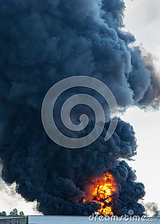 Black plumes of smoke from an accidental toxic industrial fire as seen from a behind a factory building Stock Photo