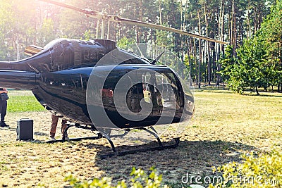 Black private modern luxury helicopter standing on grass field near forest at country rural landscape. Rich buiness lifestyle Stock Photo