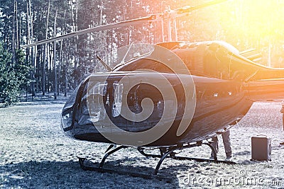 Black private modern luxury helicopter standing on grass field near forest at country rural landscape. Rich buiness lifestyle Stock Photo