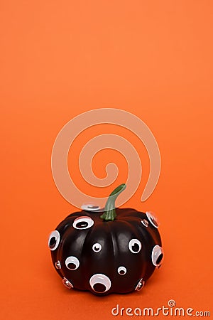 Black pumpkin with many eyes on orange background. Stock Photo