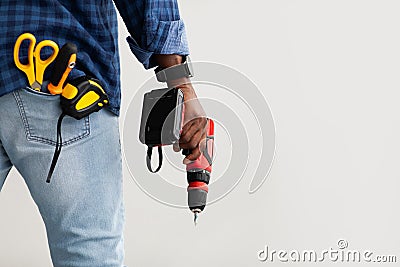 Black repairman holding electric drill in hand, in pocket measuring tape, screwdriver and scissors, copy space Stock Photo