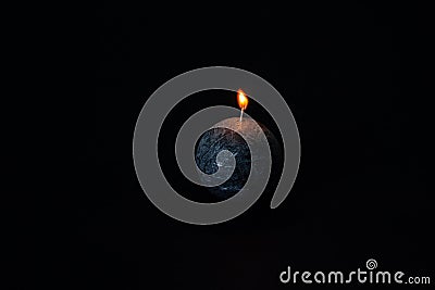 Black, round candle with texture burning isolated on black background. Stock Photo