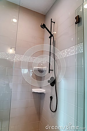 Black round shower head on tile wall of shower stall with hinged glass door Stock Photo