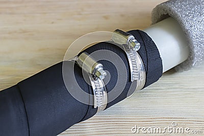 Black rubber hose connected to a polypropylene pipe by two metal clamps, on a wooden background. Stock Photo