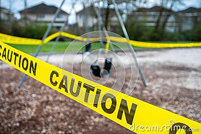 Black rubber swings in closed public playground surrounded by yellow caution tape during Corvid-19 Coronavirus pandemic Stock Photo