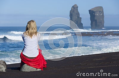 Beautiful blonde woman sits on beach stone, near to the iconic wild rock formations next to Mosteiros, in Sao Miguel island, Azore Stock Photo