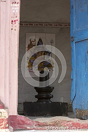 A black Shiva linga idol with Lord Shiva photo in backside in Shiva temple Stock Photo