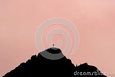 Black silhouette of mountain peak with summit cross. Rose background. Stock Photo