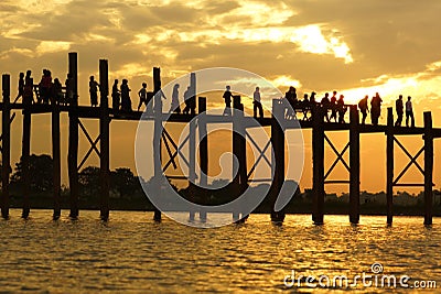 Black silhouette of teakwood U Bein Bridge and walking people on background of orange cloudy sky at sunset time, Burma Stock Photo