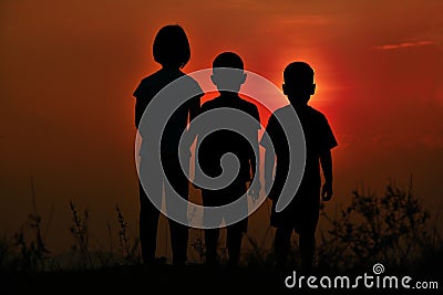 Black silhouette of three children standing together. There is a sky at sunset Stock Photo