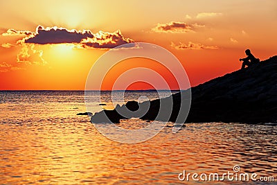 Black silhouette of young man sitting on sunset sea beach Stock Photo