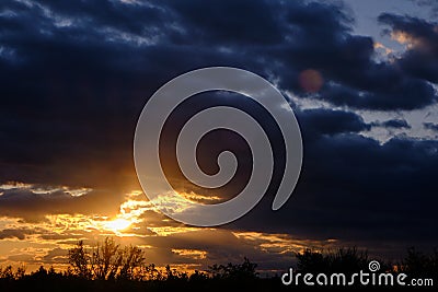 Black silhouettes trees, storm clouds with light breaking through from sun at sunset Stock Photo