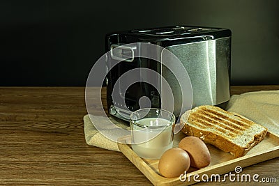 Black and silver electric micro oven with toast, fresh eggs and glass of milk on brown wooden and black blackground Stock Photo