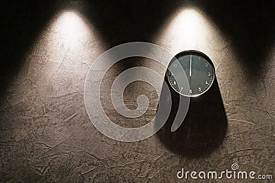 Black simple analog clock showing midnight hanging on the wall with shadows and copy space on the left Stock Photo