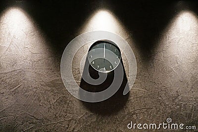 Black simple analog clock showing midnight hanging on the wall with shadows and copy space around Stock Photo