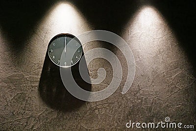 Black simple analog clock showing midnight hanging on the wall with shadows and copy space on the right Stock Photo