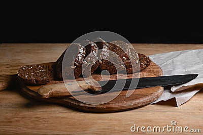 Black sliced bread on the board, vintage knife on the table and the old background, concept of healthy eating, place for text, set Stock Photo