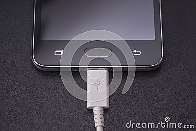 Black smartphone on black background with white cable Stock Photo